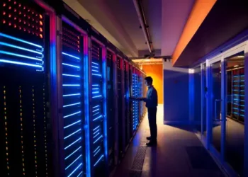 Technician monitoring server room with illuminated racks; industrial cybersecurity. - Supply Chain News