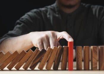 Person's hand stopping dominoes from falling, highlighting risk management for small businesses. - Supply Chain News