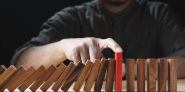 Person's hand stopping dominoes from falling, highlighting risk management for small businesses. - Supply Chain News