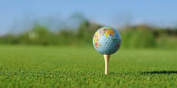 Golf ball with world map design on tee on green - Supply Chain News