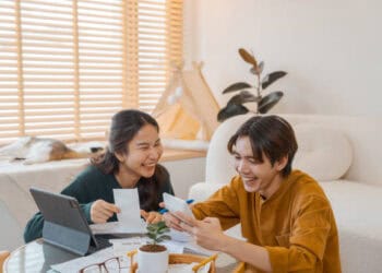 Happy young couple reviewing documents and using a tablet and phone. - Supply Chain News
