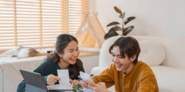 Happy young couple reviewing documents and using a tablet and phone. - Supply Chain News