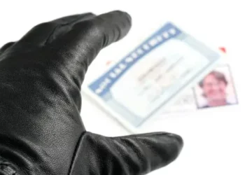 Close-up of a gloved hand reaching for an identity document; New Hampshire identity theft arrest. - Supply Chain News