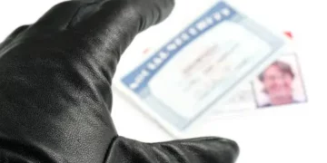 Close-up of a gloved hand reaching for an identity document; New Hampshire identity theft arrest. - Supply Chain News
