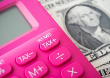 Pink calculator with tax buttons rests on US dollar bill; Tax Rate, Tax+, Tax- are visible. - Supply Chain News