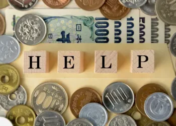 Wooden blocks spelling HELP surrounded by Japanese yen coins and banknotes. - Supply Chain News