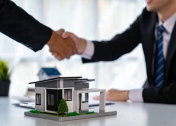 Businesspeople shaking hands over a model house, symbolizing a real estate deal. - Supply Chain News