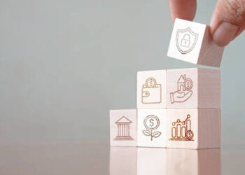 A hand is holding wooden blocks with business icons on them, showcasing the impact of US-EU trade policies in the Biden era.