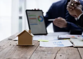 Businesspeople reviewing financial charts and a house model, symbolizing M&A in insurance brokerage. - Supply Chain News