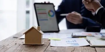 Businesspeople reviewing financial charts and a house model, symbolizing M&A in insurance brokerage. - Supply Chain News