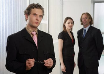 Three business professionals, two women and one man, stand in an office setting. The man is in the foreground. - Supply Chain News