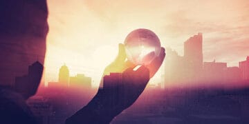 Silhouette of a hand holding a globe, superimposed over a city skyline at sunset. Global economic growth potential. - Supply Chain News