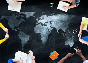 A group of people examining a world map on a chalkboard, discussing the challenges and reducing dependency.
