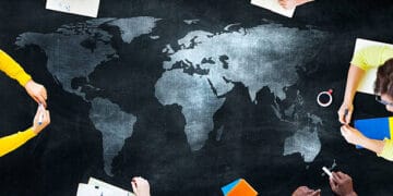 A group of people examining a world map on a chalkboard, discussing the challenges and reducing dependency.