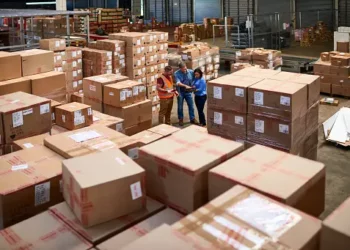 Two South-East Asian supply chain leaders standing in a warehouse full of boxes, discussing manufacturing alternatives.