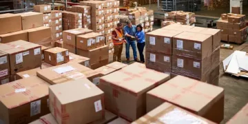 Two South-East Asian supply chain leaders standing in a warehouse full of boxes, discussing manufacturing alternatives.