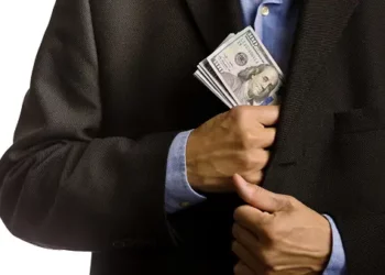 Man concealing cash in jacket pocket, illustrating potential PDAF misuse. - Supply Chain News