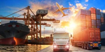 A truck is driving by a container ship during sunset, emphasizing the significance of international trade.