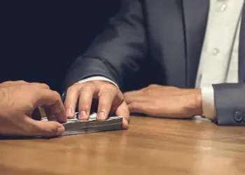 Hands exchanging cash across a table, illustrating potential social media investment fraud. - Supply Chain News