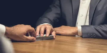 Hands exchanging cash across a table, illustrating potential social media investment fraud. - Supply Chain News