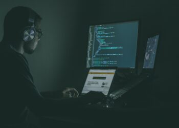 Person wearing headphones works on laptop and monitors displaying code, boosting cybersecurity skills for Moldovan SMEs. - Supply Chain News