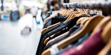 Luxury clothing on hangers in a boutique. Global luxury goods market trends 2023. - Supply Chain News