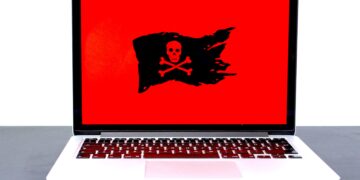 Laptop screen displays a red background with a black skull and crossbones pirate flag; ransomware attack. - Supply Chain News