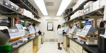 Scientist in lab coat operating semiconductor manufacturing equipment. - Supply Chain News