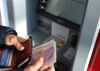 Person withdrawing cash from ATM, using a leather wallet. - Supply Chain News