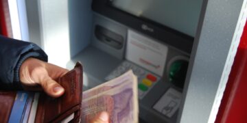 Person withdrawing cash from ATM, using a leather wallet. - Supply Chain News