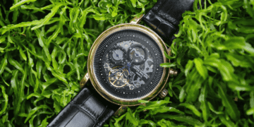 Gold Patek Philippe Geneve watch with black leather band, nestled in green foliage. - Supply Chain News
