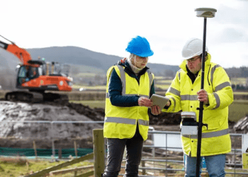 Two surveyors review data on a tablet at a construction site. Reclamation project. - Supply Chain News