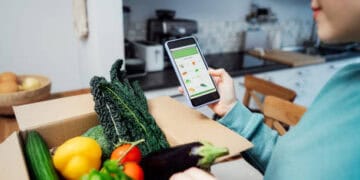 Person using smartphone to order groceries, then placing fresh produce into a box for delivery. - Supply Chain News