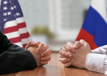 Two business people sitting at a table with American and Russian flags discussing US-Russia sanctions.
