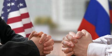 Two business people sitting at a table with American and Russian flags discussing US-Russia sanctions.