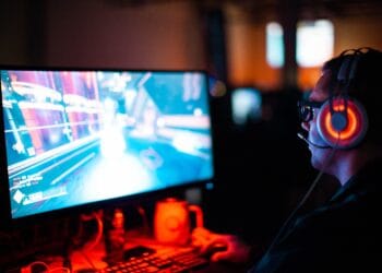 Gamer wearing headset plays video game on computer. - Supply Chain News