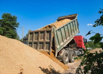 A dump truck is dumping **sand** into a pile of dirt.