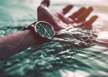 A person's hand with a luxurious watch submerged in transparent water.