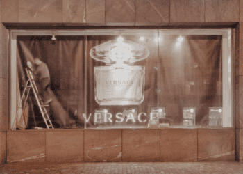 Nighttime view of a Versace Bright Crystal perfume display in a store window. A worker adjusts the display. - Supply Chain News