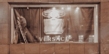 Nighttime view of a Versace Bright Crystal perfume display in a store window. A worker adjusts the display. - Supply Chain News