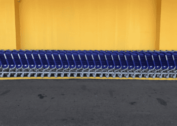 Row of blue shopping carts parked against a yellow wall. - Supply Chain News