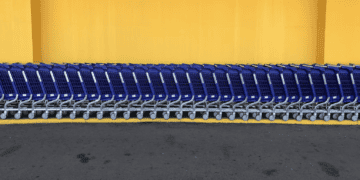 Row of blue shopping carts parked against a yellow wall. - Supply Chain News