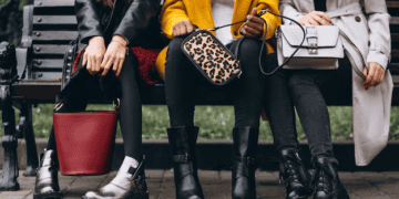 Three women wearing boots and stylish handbags sit on a park bench. Luxury fashion accessories. - Supply Chain News