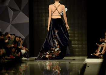 Model showcasing a high-fashion gown at a runway show. The dress features floral embroidery. - Supply Chain News