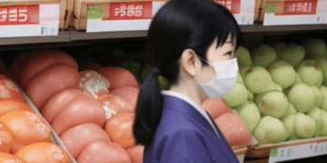 In a Japanese supermarket, a woman wearing a surgical mask navigates through the aisles amidst rising food prices due to inflation.