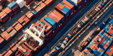 Aerial view of a container ship at a busy port, illustrating global trade and supply chain logistics. - Supply Chain News