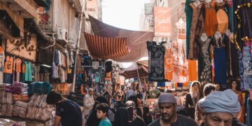 Busy Egyptian market street scene under striped awnings. People shop for clothing and goods. - Supply Chain News