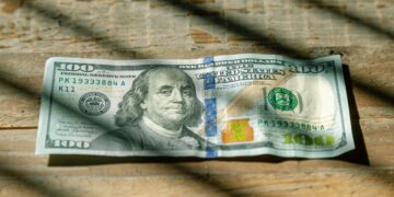 A one hundred dollar bill on a wooden table, representing US Federal Reserve Rate Cuts.