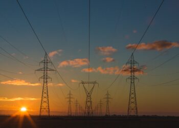 High voltage pylons illuminated by the vibrant colors of a sunset, symbolizing the surge in clean energy minerals market.