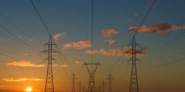 High voltage pylons illuminated by the vibrant colors of a sunset, symbolizing the surge in clean energy minerals market.
